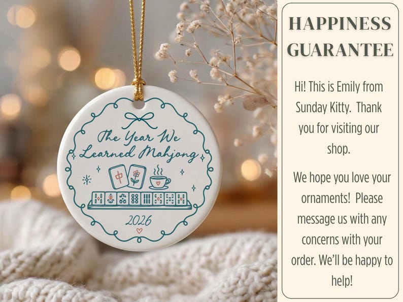 May include: A round white ceramic ornament hanging from a gold string. The front features a teal scalloped border, the text "The Year We Learned Mahjong", illustrations of mahjong tiles and a teacup, and the year "2026" with a small heart.