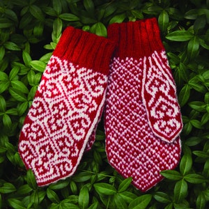 Red and white colorwork mittens on a bed of green leaves