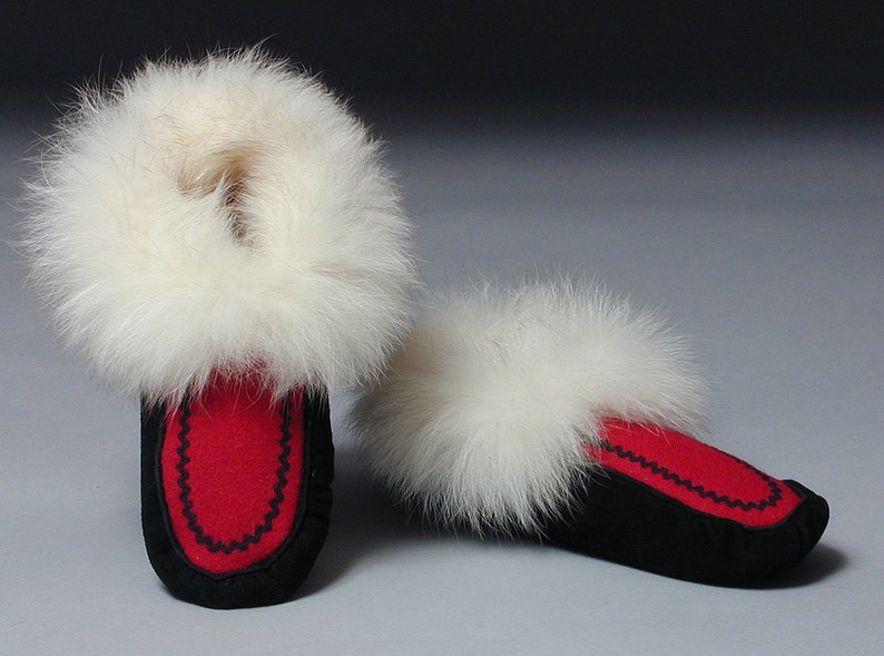 A photo of women’s moccasins made with black leather with red vamps and white fur trim
