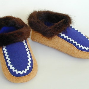 May include: A pair of brown fur-lined moccasins with blue felt uppers and white zig-zag stitching around the edges.