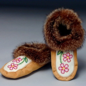 May include: A pair of white moccasins with pink flower embroidery and brown fur trim.