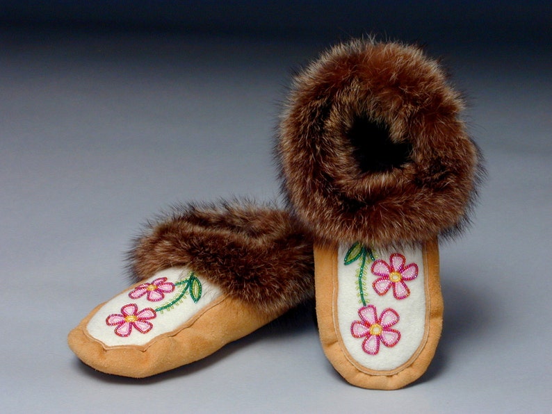 May include: A pair of white moccasins with pink flower embroidery and brown fur trim.