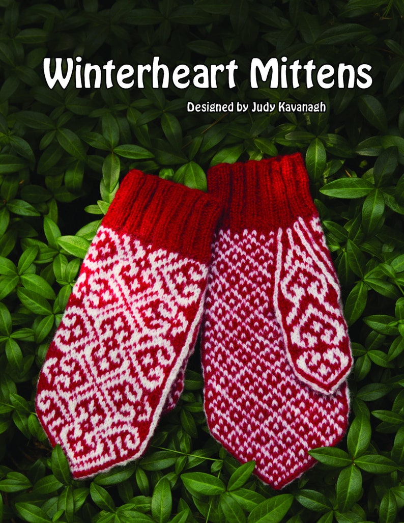Red and white colorwork mittens on a bed of green leaves