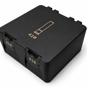 May include: A black rectangular box with a gold-colored graphic of a bullet and the number "410" printed on the front. The box has a matte finish and a hinged lid with a secure latching mechanism.