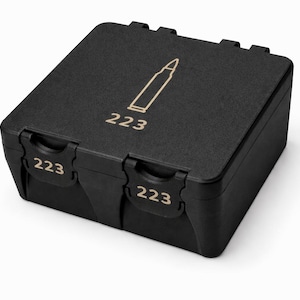 May include: A black, rectangular storage box with a hinged lid. The box features the number "223" in white on the front and sides, along with a stylized bullet graphic and the number "223" on the top. The box is designed for ammunition storage.