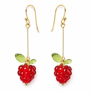 May include: A pair of gold-colored dangle earrings. Each earring features a cluster of red beads resembling a raspberry, with two green leaf accents. The earrings have a long, straight gold bar and a hook closure.