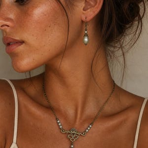 Pode incluir: Um conjunto de joias composto por um colar e um brinco. O colar apresenta uma corrente em tom de bronze com pequenas p&eacute;rolas cinzentas e um pendente central de bronze ornamentado com uma p&eacute;rola cinzenta pendente a combinar.