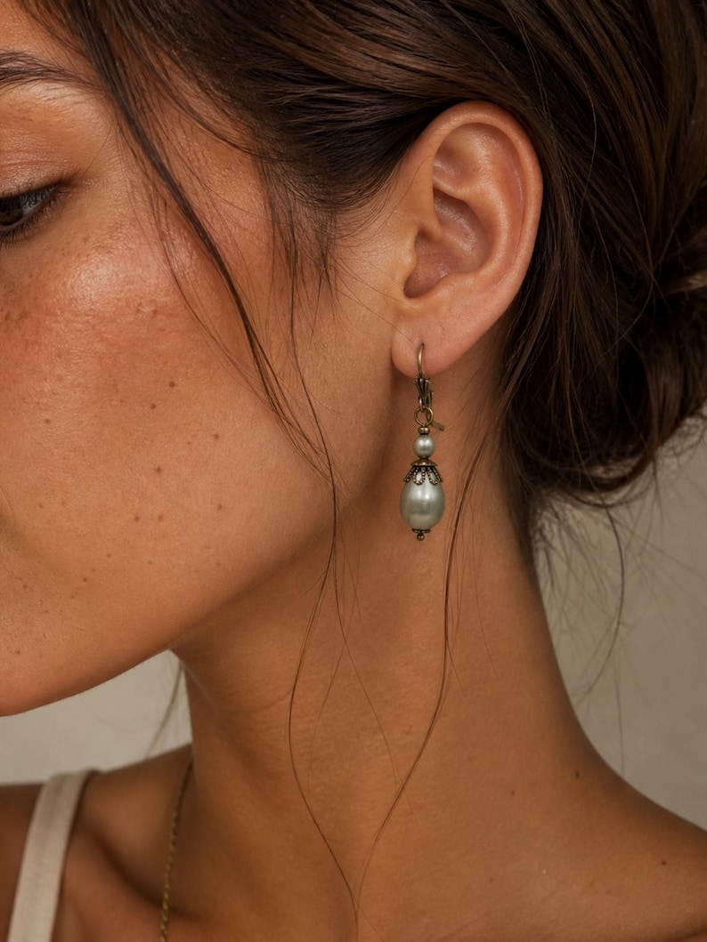 Pode incluir: Um brinco pendente com uma conta lisa em forma de gota na cor verde s&aacute;lvia, suspensa por um gancho de metal em tom de bronze. A conta &eacute; acentuada com uma pequena conta redonda a condizer e uma tampa de metal decorativa.