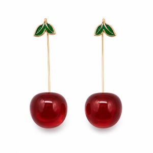 May include: A pair of drop earrings featuring two glossy, deep red cherry-shaped pendants suspended from thin gold-toned stems. Each stem is topped with a small, vibrant green enamel leaf detail, creating a realistic fruit-inspired design.