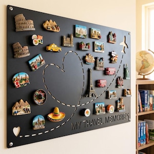 Op de afbeelding: Een rechthoekig zwart magneetbord met een lasergesneden hartvorm en een stippellijn van een vliegroute die eindigt in een vliegtuigsilhouet. Het bord is versierd met diverse kleurrijke reismagneten en bevat de tekst MY TRAVEL MEMORIES.
