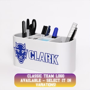 Könnte beinhalten: Ein weißer Schreibtisch-Organizer mit mehreren Fächern, der Stifte, Marker, eine Schere und ein Lineal enthält. Die Vorderseite zeigt eine blaue Grafik eines Teufelsmaskottchens und den Text CLARK. Darunter steht der Text CLASSIC TEAM LOGO AVAILABLE - SELECT IT IN VARIATIONS.