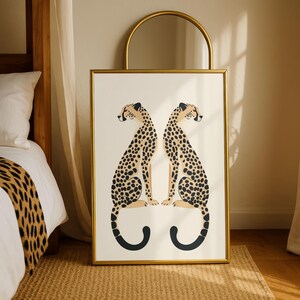 May include: A framed art print featuring two stylized cheetahs facing each other. The cheetahs have tan bodies with black spots and are set against a cream background. The frame is gold, and the artwork is displayed in a bedroom setting.