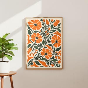 Op de afbeelding: Een ingelijste kunstafdruk met een bloemenontwerp. Het kunstwerk toont oranje bloemen en groene bladeren tegen een crèmekleurige achtergrond. De botanische illustratie heeft een vintage esthetiek, met een houten frame. De print hangt aan een witte muur.
