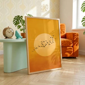 Könnte beinhalten: Ein rechteckiger gerahmter Wandkunstdruck mit einem orangefarbenen Farbverlaufshintergrund und einem großen hellgelben Kreis in der Mitte. Eine Schar kleiner schwarzer Vögel ist in einer diagonalen Formation über der Kreisform abgebildet.
