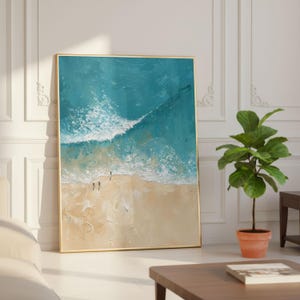 Puede incluir: Pintura abstracta enmarcada que representa una escena de playa con agua turquesa y olas blancas que se encuentran con una orilla arenosa. Dos pequeñas figuras están en la playa. La obra de arte está en un marco dorado.