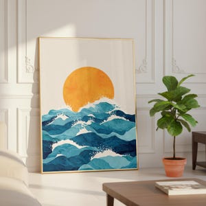 Puede incluir: Una impresión artística enmarcada que presenta una escena oceánica abstracta con un gran sol naranja que se pone sobre olas azules. La obra de arte tiene un marco dorado y se exhibe en una habitación bien iluminada con una planta y una mesa de centro.