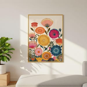 May include: A framed floral art print featuring a vibrant array of stylized flowers in shades of pink, orange, yellow, and blue. The artwork has a gold frame and is displayed against a white wall, with a glimpse of a plant and a couch in the background.