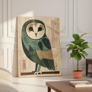 Op de afbeelding: Een ingelijste kunstdruk met een gestileerde uil-illustratie. De uil is afgebeeld in tinten groen, beige en bruin tegen een getextureerde achtergrond. Het kunstwerk is ingelijst in een goudkleurige lijst en leunt tegen een witte muur.