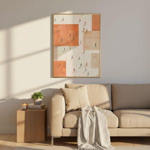 May include: An abstract framed art print featuring a geometric design with orange and beige blocks. Small figures are depicted walking within the blocks. The artwork is displayed above a beige sofa with pillows and a blanket, next to a wooden side table.