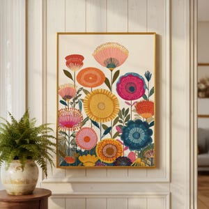 May include: A framed floral art print featuring a vibrant array of stylized flowers in shades of pink, orange, yellow, and blue. The artwork has a gold frame and is displayed against a cream-colored background. A fern in a decorative pot is in the foreground.