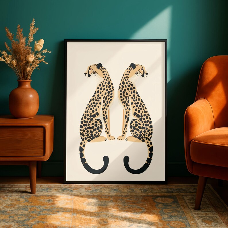 May include: A framed art print featuring two stylized cheetahs facing each other. The cheetahs have tan bodies with black spots and are set against a cream background. The frame is black, and the print is displayed in a room with teal walls and an orange chair.