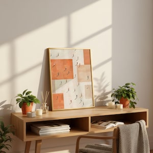 May include: A framed art print with a gold frame, featuring an abstract design of people walking on geometric shapes in shades of orange and beige. The artwork is displayed on a wooden console table with potted plants and candles.