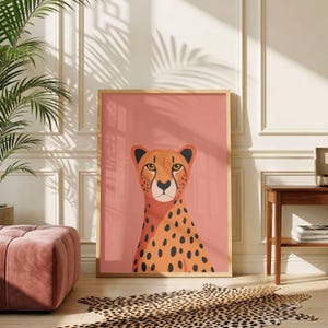 May include: A rectangular framed wall art print featuring a stylised illustration of a cheetah head and neck centred against a solid dusty rose background. The cheetah is orange with black spots and distinct black tear marks under its eyes.