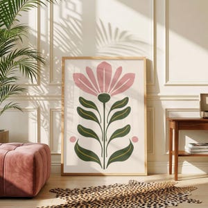Può includere: Una stampa artistica da parete rettangolare in una cornice di legno chiaro con un'illustrazione centrata di un grande fiore rosa con foglie verde scuro su sfondo crema, fiancheggiata da due piccoli cerchi rosa ai lati del gambo.