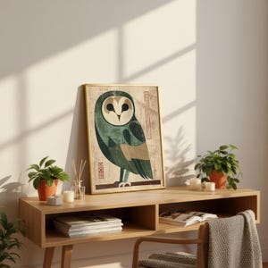 Op de afbeelding: Een ingelijste kunstprint met een gestileerde uil-illustratie in groen, beige en bruin. Het kunstwerk heeft een vintage esthetiek, met een gouden lijst. De print wordt getoond op een houten console, samen met potplanten en kaarsen.
