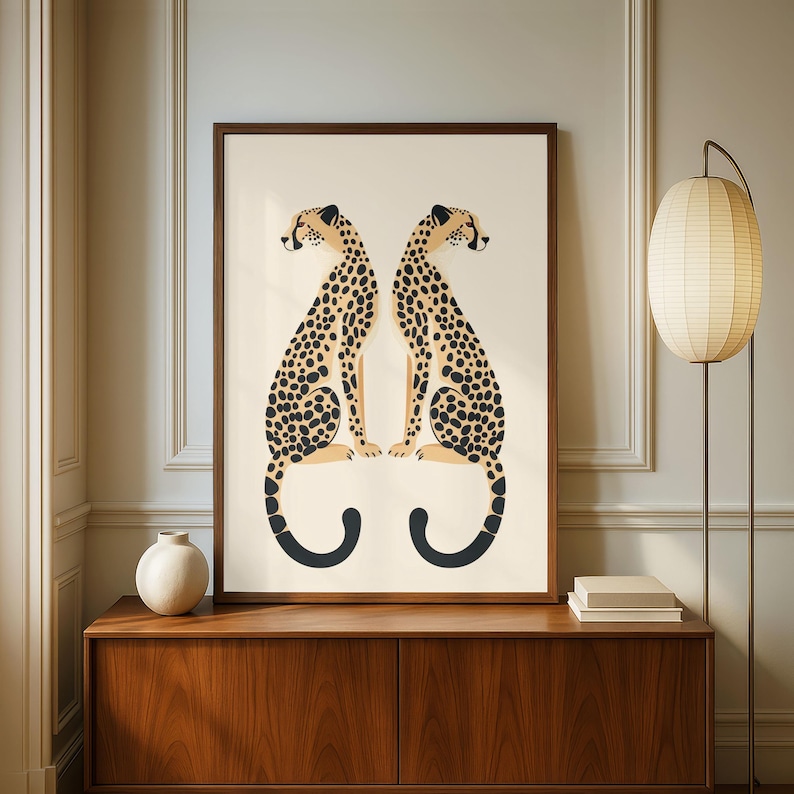 May include: A framed art print featuring two stylized cheetahs facing each other. The cheetahs have tan fur with black spots and black tails. The artwork is set against a cream background and framed in a dark brown wood.