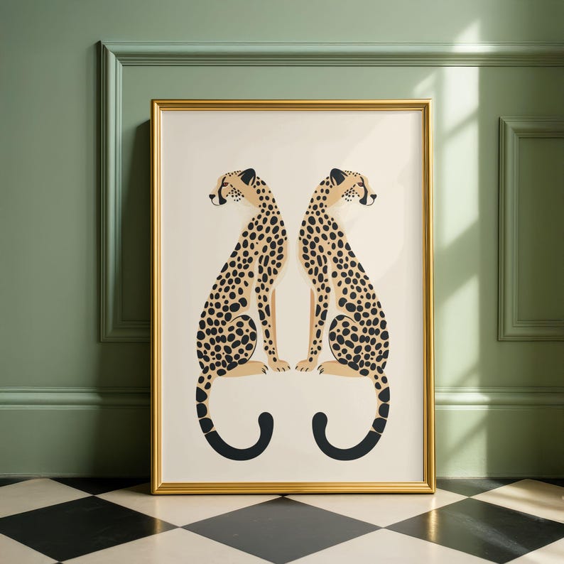 May include: A framed art print featuring two stylized cheetahs facing each other. The cheetahs have tan bodies with black spots and black tails. The artwork is set against a cream background, framed in gold, and leans against a green wall.