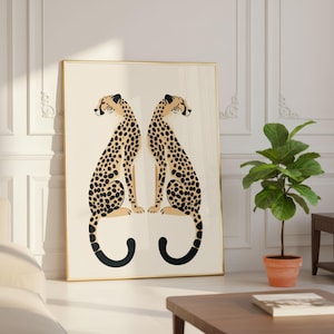 May include: A framed art print featuring two stylized cheetahs facing each other. The cheetahs have tan bodies with black spots and black curved tails. The background is off-white, and the frame is gold.