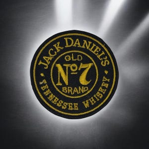 Può includere: Una toppa ricamata circolare con sfondo nero e filo color oro. Il testo recita Jack Daniel's Old No. 7 Brand Tennessee Whiskey in una disposizione circolare, con il logo No. 7 ben visibile al centro della toppa ricamata in modo dettagliato.