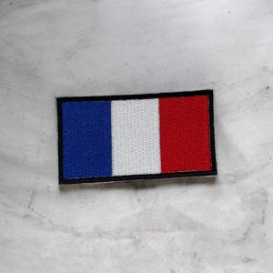 May include: A rectangular embroidered patch featuring the French national flag design with vertical stripes in blue, white, and red. The patch is finished with a solid black stitched border that frames the tricolour pattern clearly.