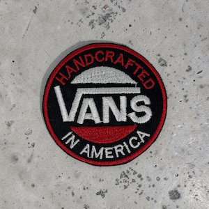 Könnte beinhalten: Ein kreisförmiger gestickter Aufnäher mit schwarzem Hintergrund und rotem Rand. In der Mitte befindet sich der weiße Schriftzug VANS mit einer horizontalen Linie darüber. HANDCRAFTED ist oben und IN AMERICA unten in weißen Buchstaben gebogen.