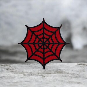 Peut inclure: Un écusson de toile d'araignée rouge avec des détails noirs. Le patch est brodé avec un motif de toile détaillé et un bord noir. Un accessoire sur le thème d'Halloween ou gothique.
