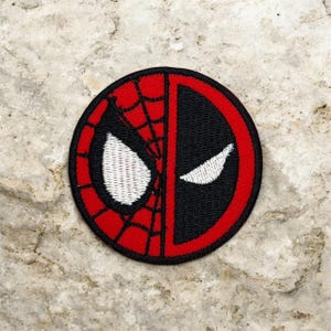 May include: A round, embroidered patch featuring a split design. One half showcases Spider-Man's web pattern in red and black, with a white eye. The other half is black with a white eye, representing Deadpool. The patch has a red border.