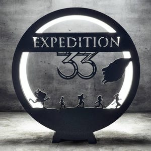 Op de afbeelding: Zwart metalen Expedition 33-bord met een cirkelvormig ontwerp. Het bord toont het woord "EXPEDITION" boven het nummer "33" en silhouetten van rennende mensen. Het bord is van achteren verlicht.