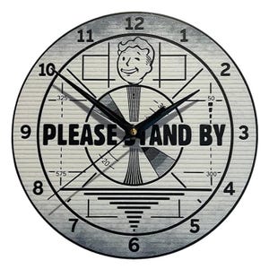 May include: Round wall clock with a gray and white design. The clock face features a retro television test pattern, the words "PLEASE STAND BY," and a cartoon character. Black clock hands indicate the time.