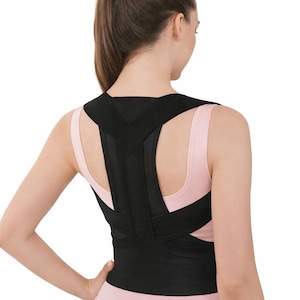 Puede incluir: Corrector de postura negro usado por una persona, visto desde atrás. El corrector presenta correas que se cruzan sobre los hombros y la espalda, y una banda ancha alrededor de la cintura. La persona lleva una camiseta rosa.