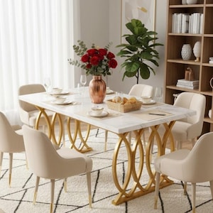 Op de afbeelding: Een moderne eethoek met een tafel met een wit marmeren blad en een gouden geometrische basis, omringd door zes beige gestoffeerde stoelen. Een vaas met rode rozen staat op de tafel, met een tapijt en een boekenrek op de achtergrond.