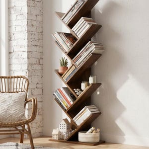 Op de afbeelding: Een donkerbruine, boomvormige boekenplank gevuld met boeken, kaarsen en decoratieve items. De boekenplank is gemaakt van hout en heeft schuine planken. Een rieten stoel en een patroonkleed staan op de voorgrond.