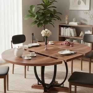 May include: A round, extendable wooden dining table with a dark brown finish. The table has a black metal base and is set with plates, cups, and a teapot. The room features chairs, a plant, and a bookshelf.