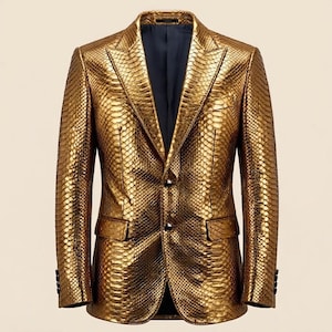 Puede incluir: Una americana de color dorado metálico con un patrón texturizado de piel de serpiente en todo el exterior. La prenda incluye solapas de muesca, dos botones frontales, dos bolsillos con solapa y un forro interior oscuro visible en el cuello.