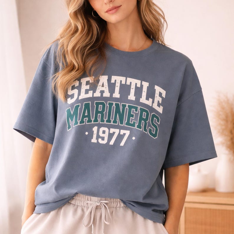 May include: A blue t-shirt with the text "SEATTLE MARINERS 1977" in white and teal lettering. The shirt has short sleeves and a crew neck. The shirt is made of a soft material.