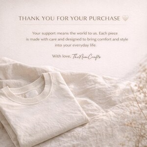 May include: A cream-colored t-shirt is neatly folded on a textured, off-white fabric. The image includes text that reads "THANK YOU FOR YOUR PURCHASE" and a message about comfort and style. The brand name "The Nom Crafts" is also visible.