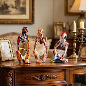 May include: Three abstract sculptures in a seated pose, with hands to the face. The sculptures are painted with vibrant colors including blue, orange, red, and white. They are displayed on a dark wood cabinet.
