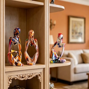 May include: Three colorful abstract human figure sculptures. The sculptures are painted with vibrant colors including blue, orange, red, and yellow. They are displayed on a wooden shelf in a living room setting.