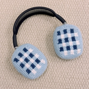 May include: Over-ear headphones with light blue crochet ear covers featuring a checkered pattern in white and navy blue. The headband is black with a padded top, and the earcups are silver.