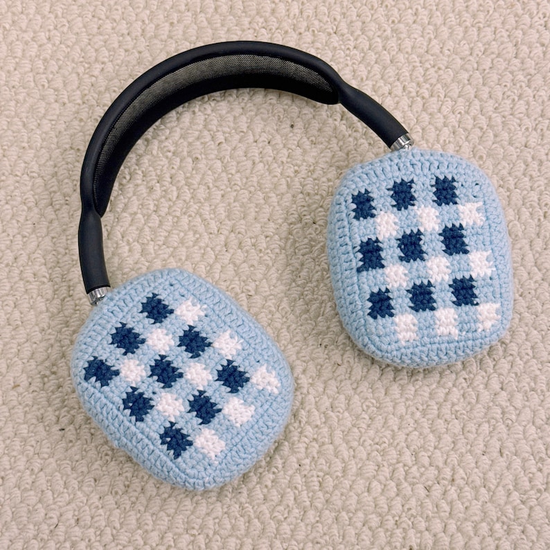 May include: Over-ear headphones with light blue crochet ear covers featuring a checkered pattern in white and navy blue. The headband is black with a padded top, and the earcups are silver.